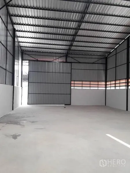 货栈 出租在Lam Luk Ka, Pathum Thani - 开阔存储区，面向大型金属卷闸门与带通风的墙板。