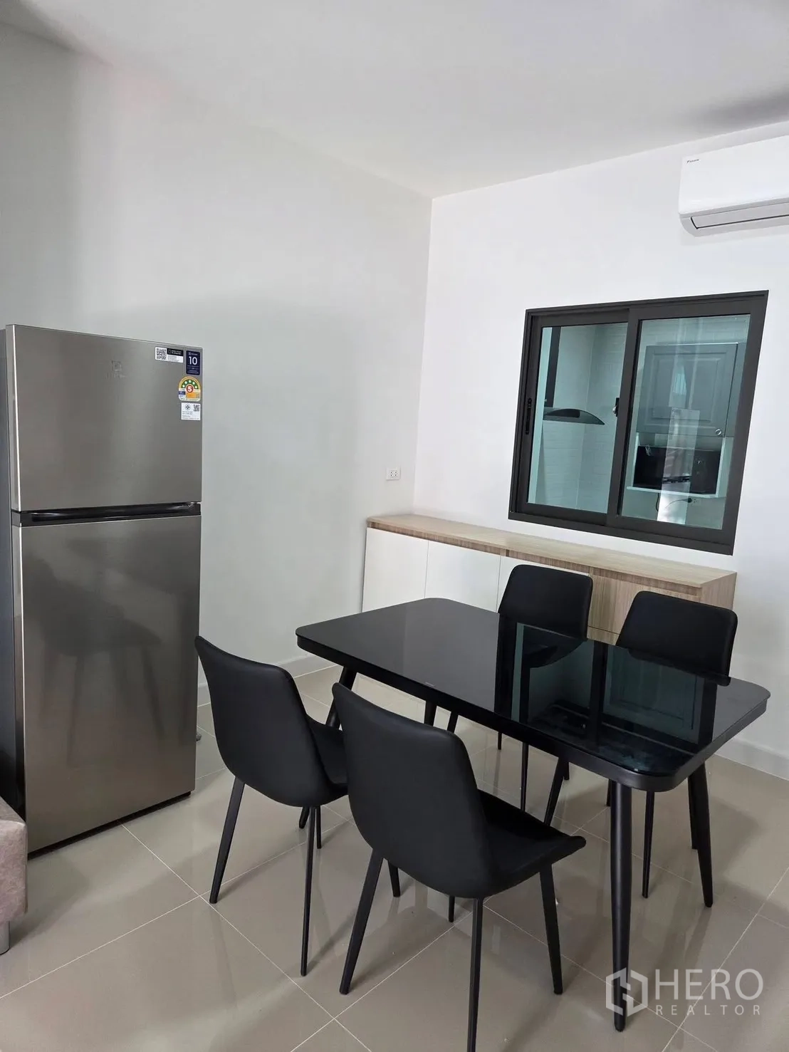 Townhouse for rent in Bang Phli, Samut Prakan - Dining area with black glass-top table and four chairs next to a stainless fridge and air conditioner.