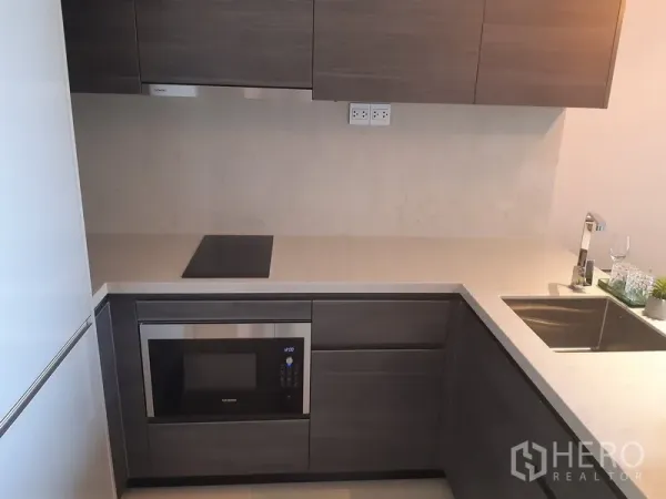 คอนโด ให้เช่าหรือขายในWatthana, Bangkok - ครัวรูปตัว U โทนเทา พร้อมตู้บิวท์อิน เตาไฟฟ้า ไมโครเวฟ และอ่างล้างจานสแตนเลส