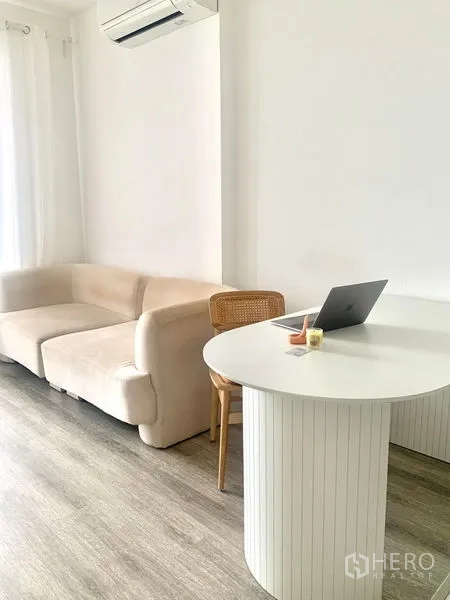 Condominium for sale in Bang Na, Bangkok - Living-dining space with cream sofa and rounded table under air conditioning.