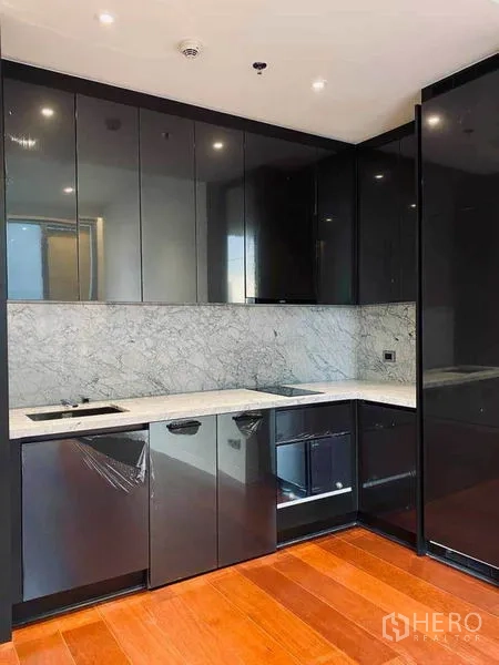 Condominium for sale in Watthana, Bangkok - L-shaped modern kitchen with built-in appliances, glossy cabinets, and marble countertop.