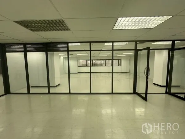 办公空间 出租在Phaya Thai, Bangkok - 通过通高玻璃隔断看到的大型工作区，配网格吊顶灯。