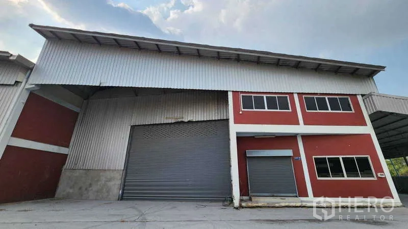 Warehouse for rent in Nonthaburi - Front view of high-clearance warehouse with twin roller shutter doors next to a two-storey office facade.