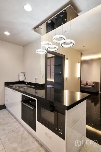 Condominium for sale in Ratchathewi, Bangkok - Modern kitchen peninsula with black stone countertop, pendant lights and built-in oven and microwave.