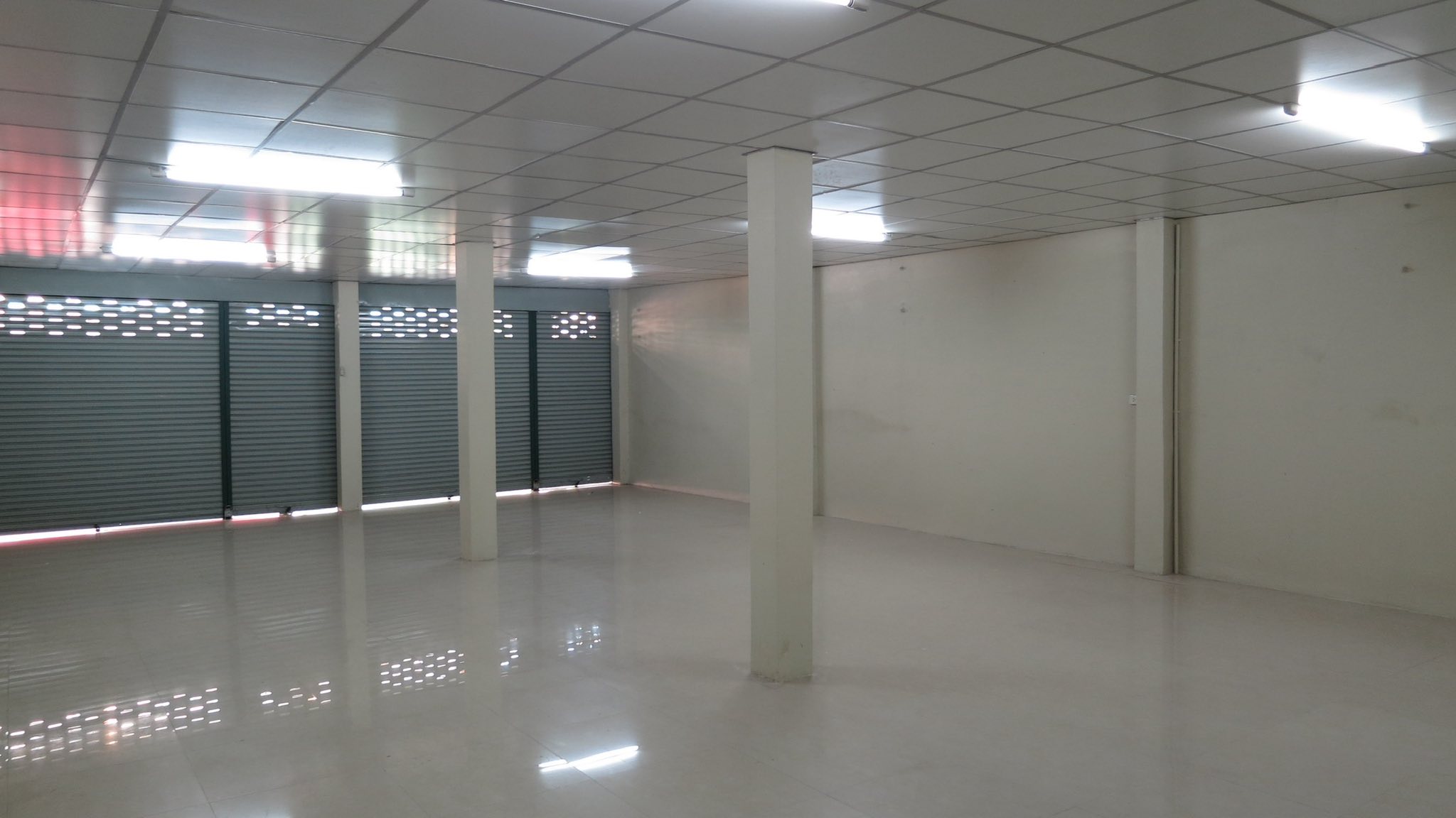 Warehouse for rent in Wang Thonglang, Bangkok - Wide hall with tiled floor and closed roller shutters along the frontage.