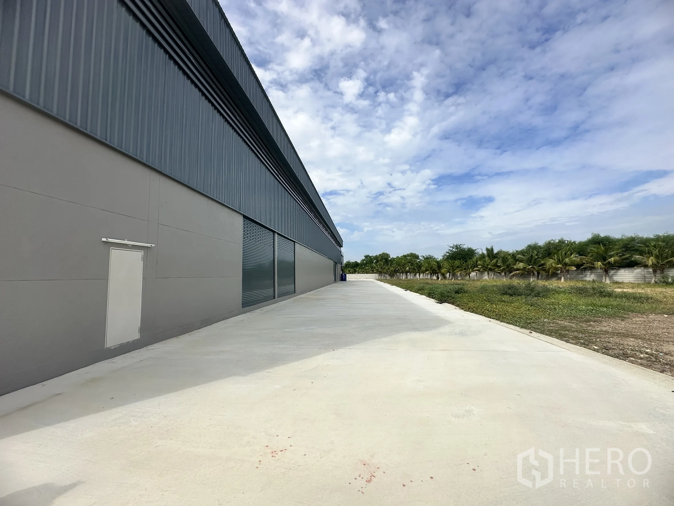 Factory for rent or sale in Bang Len, Nakhon Pathom - Side elevation of the warehouse with roller shutters, metal cladding, and a service door opening to a broad access road.