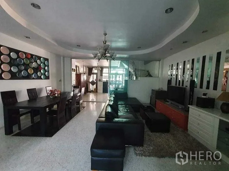 Townhouse for rent or sale in Bang Kho Laem, Bangkok - Living room with black sectional sofa, dining table and colorful plate artwork.