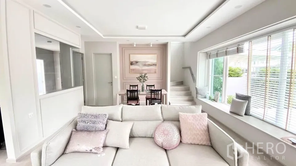 联排别墅 出租在Prawet, Bangkok - 自然采光充足的客厅，大窗、沙发、电视墙及楼梯。