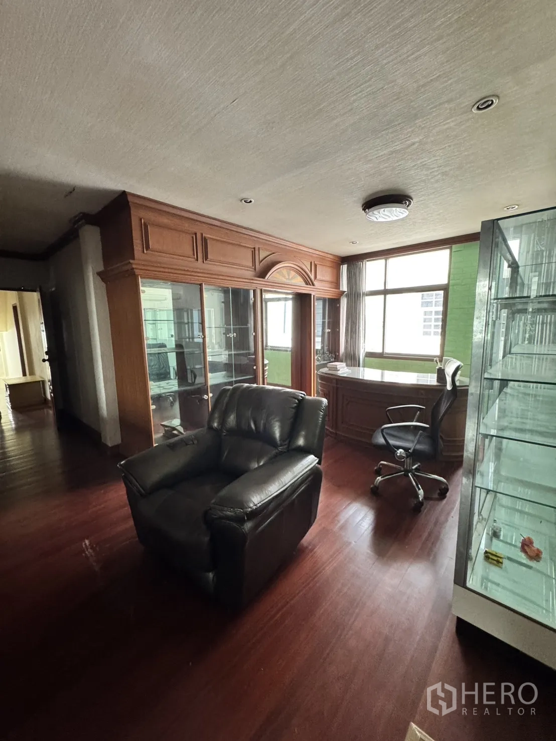 Home Office for rent in Watthana, Bangkok - Executive office room with bay window, leather armchair, desk, and glass display cabinets.