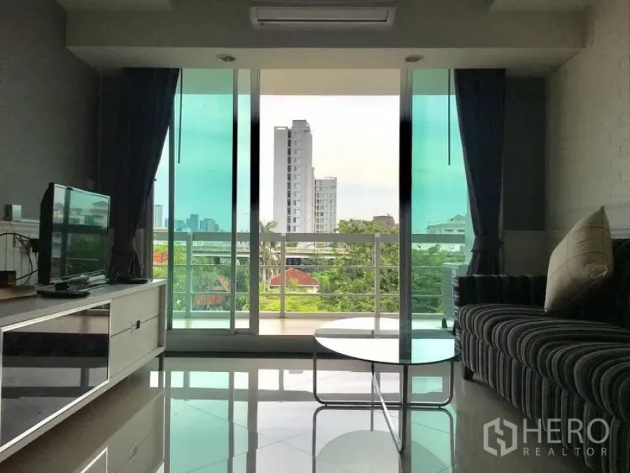 คอนโด ให้เช่าในKhlong Toei, Bangkok - ห้องนั่งเล่นสว่าง โซฟาลายทาง ตู้ทีวี และระเบียงชมวิวเมืองและต้นไม้เขียวขจี