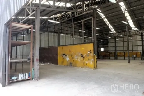 Warehouse for rent in Pak Kret, Nonthaburi - Entry view of the warehouse with a metal shelving unit and yellow divider wall.