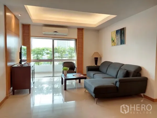 Apartment for rent - Living room with L-shaped sofa, large window and balcony overlooking greenery.