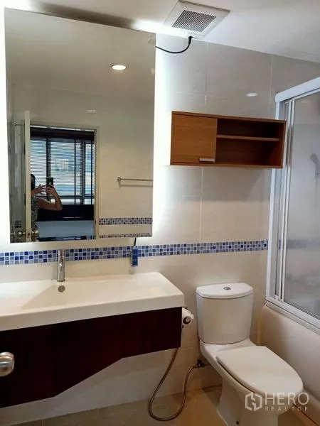 Condominium for rent in Bang Rak, Bangkok - Modern bathroom with large mirror, vanity, toilet and glass shower enclosure.