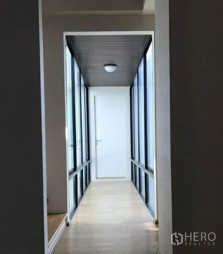 Detached House for sale in Suan Luang, Bangkok - Glass-sided corridor with wooden floor leading to an interior white door.