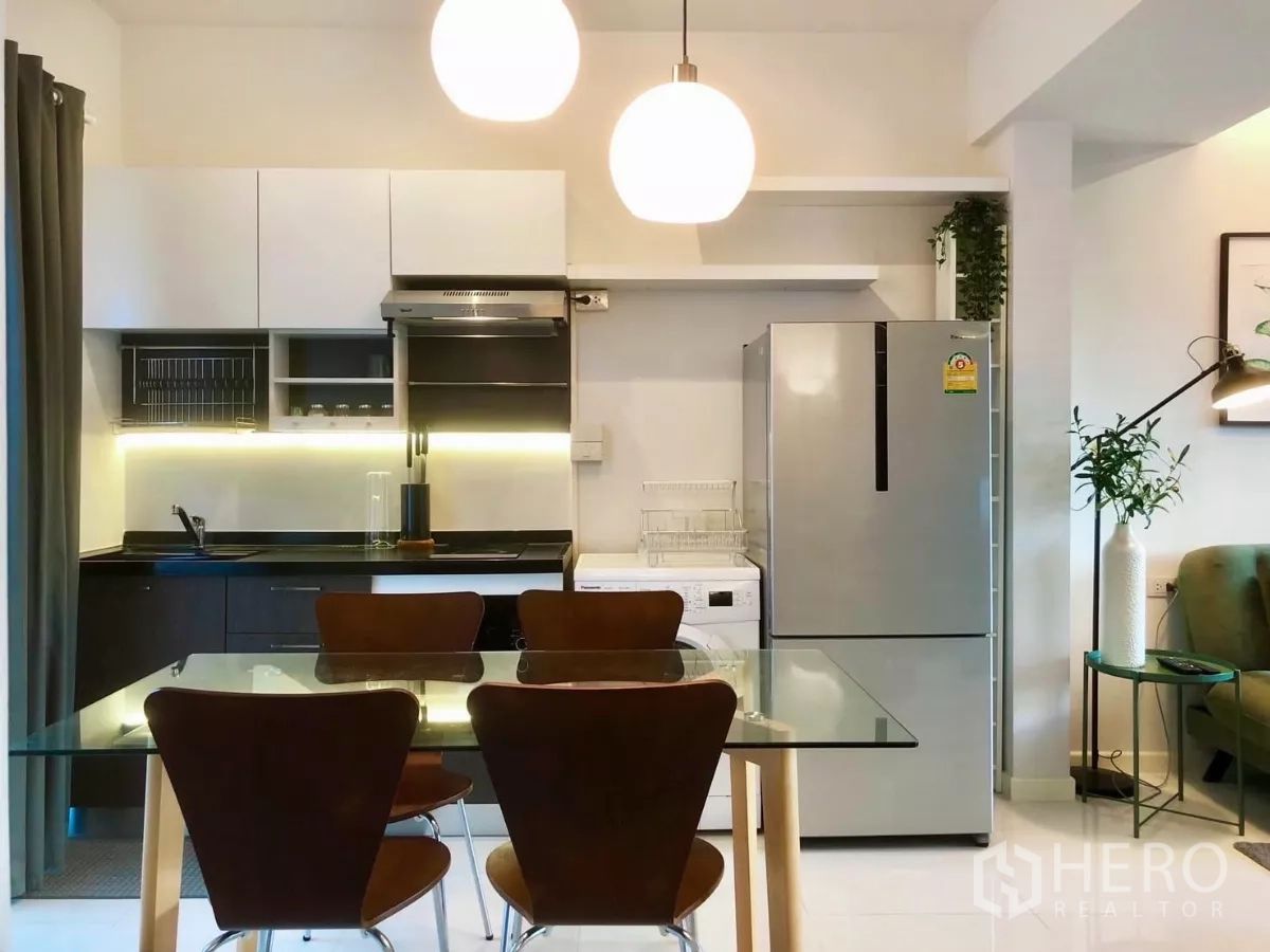 Townhouse for rent or sale in Bang Phli, Samut Prakan - Open-plan kitchen with glass dining table, pendant lights, and stainless fridge.