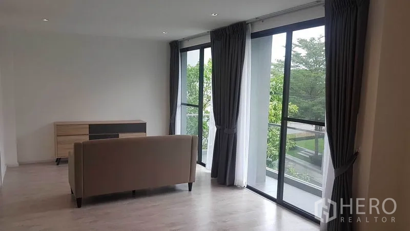 Detached House for rent in Prawet, Bangkok - Upper-floor family room with sofa and full-height windows opening to balcony views.