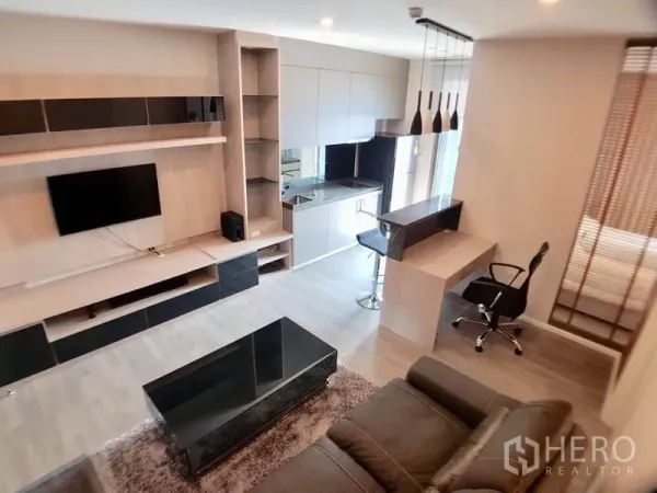 Condominium for sale in Watthana, Bangkok - Modern open-plan living room with built-in TV wall, sofa, and compact kitchen with breakfast bar in a Bangkok condo.