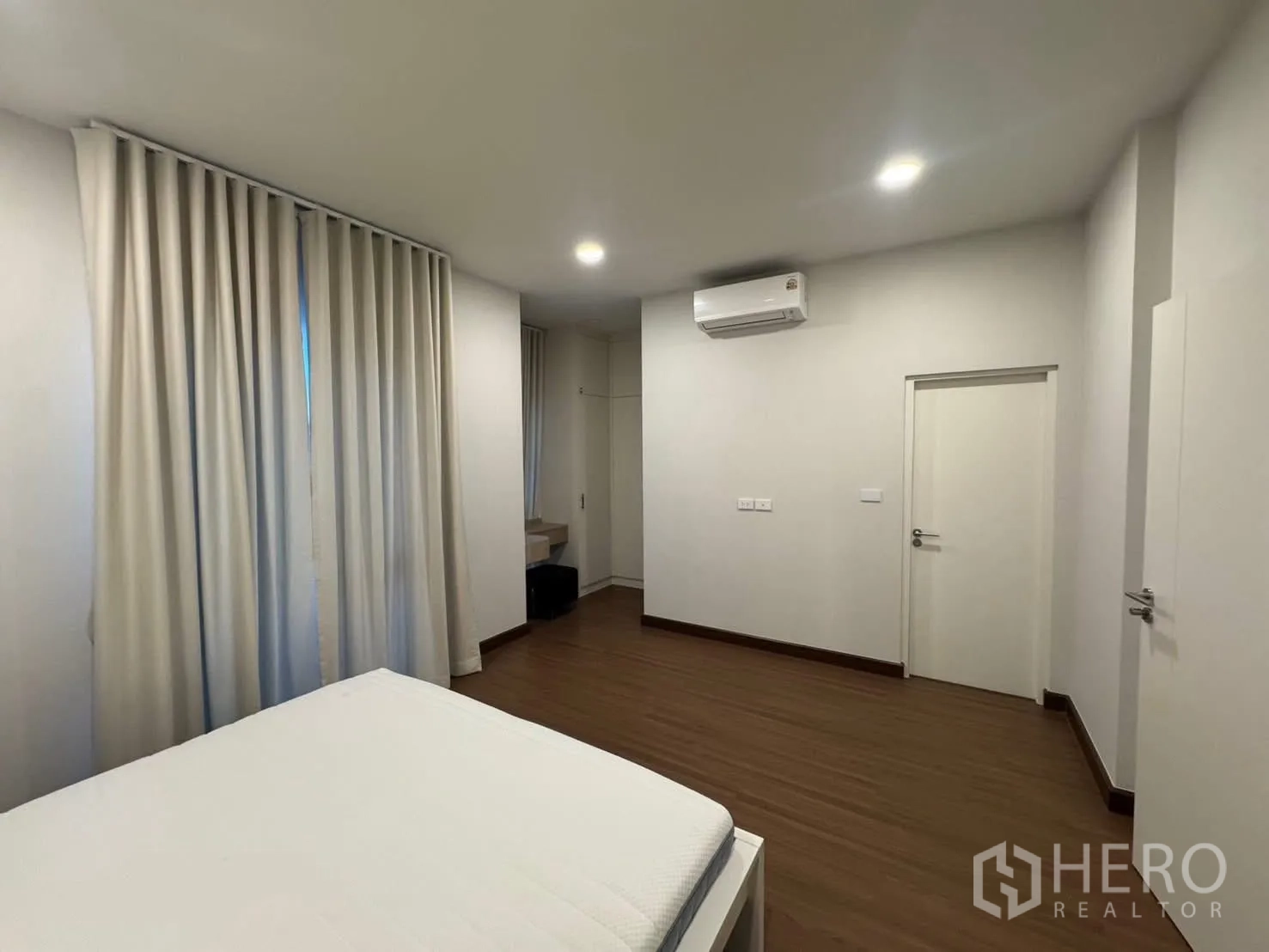 Detached House for rent in Bang Phli, Samut Prakan - Large bedroom with white curtains, wall air conditioner, and wood floors.