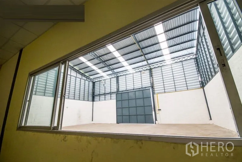 คลังสินค้า ให้เช่า - มุมมองจากหน้าต่างออฟฟิศภายในสู่พื้นที่คลังสินค้าและประตูเข้า