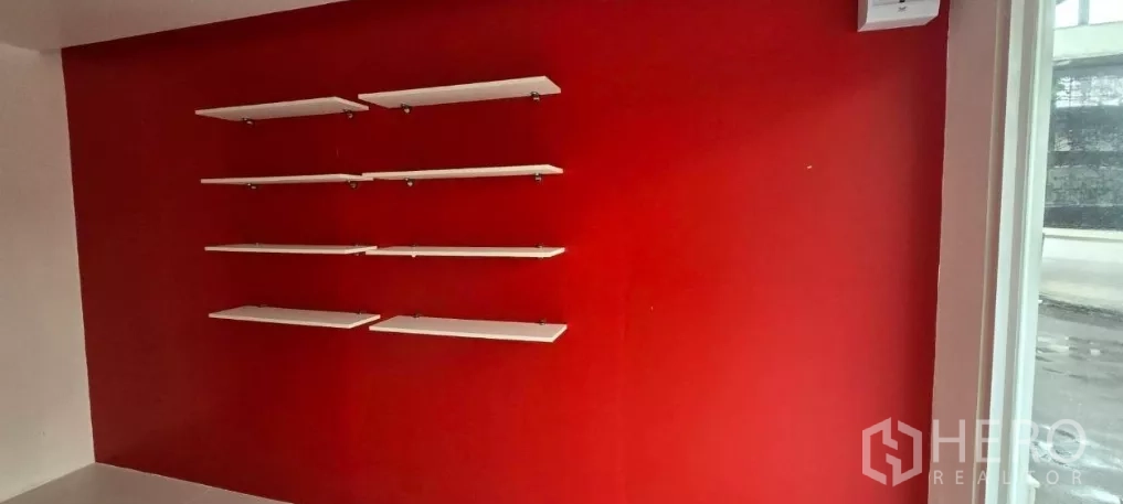 พื้นที่ขายของ for rent in Watthana, Bangkok - ผนังสีแดงติดตั้งชั้นโชว์สินค้าลอยสีขาวหลายชั้น ใกล้หน้าต่างร้าน