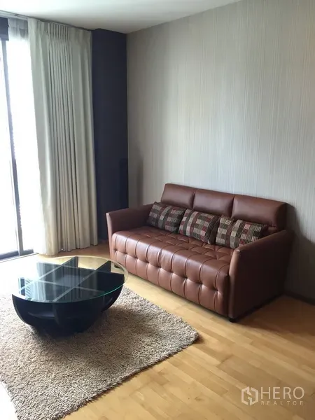 公寓 出租或出售在Khlong Toei, Bangkok - 温馨客厅，棕色皮沙发、玻璃茶几与落地窗帘。