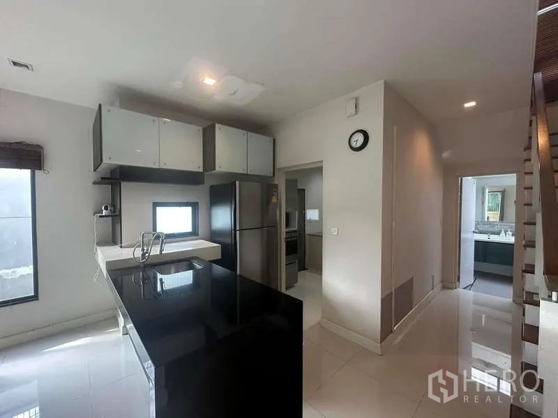 Detached House for rent or sale in Bang Kapi, Bangkok - Open-plan kitchen with black island countertop, upper cabinets, refrigerator and view to stairway.