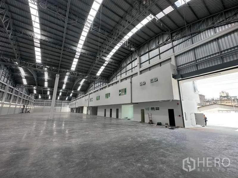 Factory for rent in Khlong Luang, Pathum Thani - Expansive warehouse interior with high arched steel roof, skylights and attached office block.