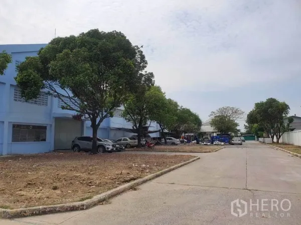 货栈 出租在Nakhon Pathom - 园区内部道路，两侧有树木与仓库旁停车位。