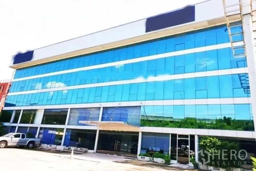 办公空间 出租在Suan Luang, Bangkok - 现代写字楼外观，蓝色玻璃幕墙与地面停车位。