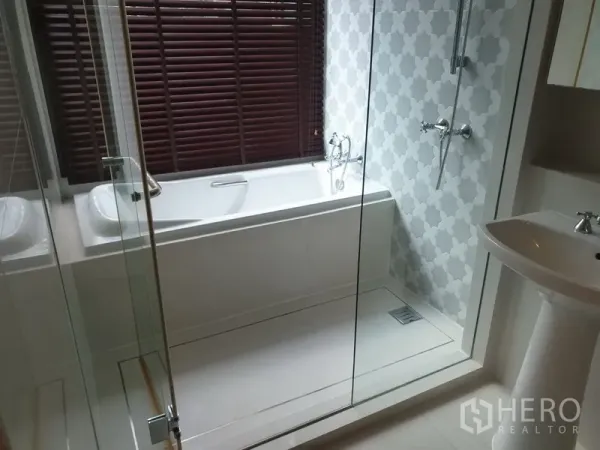 Condominium for rent in Khlong Toei, Bangkok - Contemporary bathroom with glass-enclosed shower, separate bathtub, patterned wall tile, and pedestal sink.