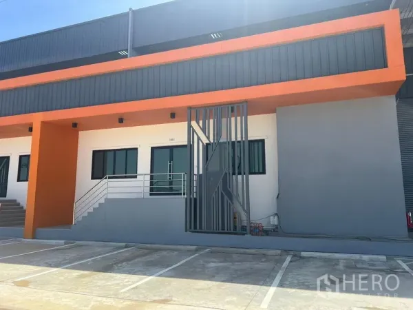 Factory for rent in Bang Pakong, Chachoengsao - Modern factory facade with orange accents, office windows, stairs and marked parking bays.