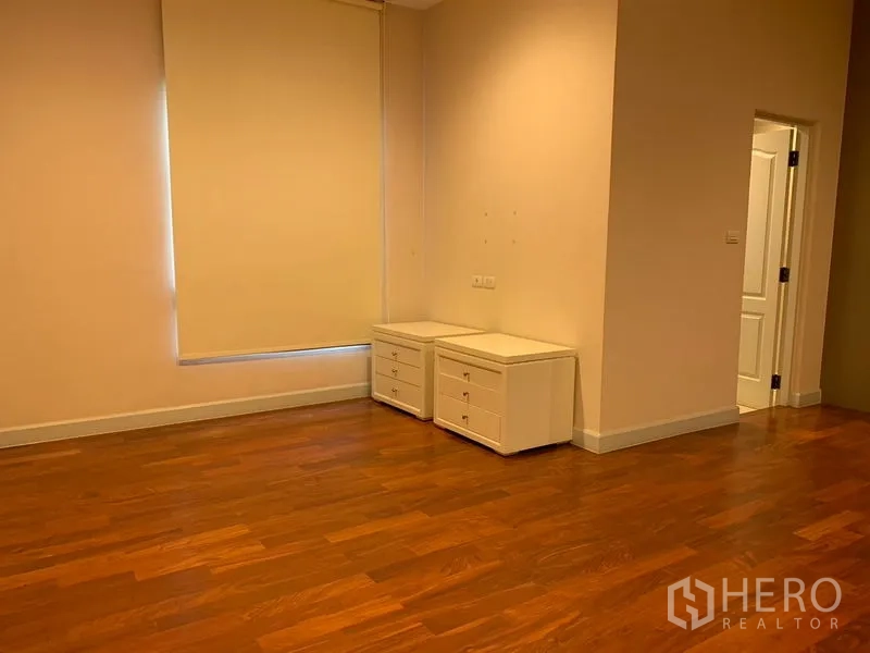 Detached House for rent or sale in Khan Na Yao, Bangkok - Empty bedroom with warm wood flooring, roller blinds and two white side cabinets.