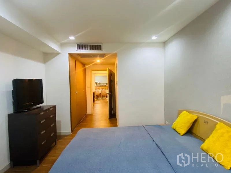Condominium for rent in Watthana, Bangkok - Bedroom with TV on dresser, built-in wardrobes and a view through the hallway toward the kitchen and dining area.