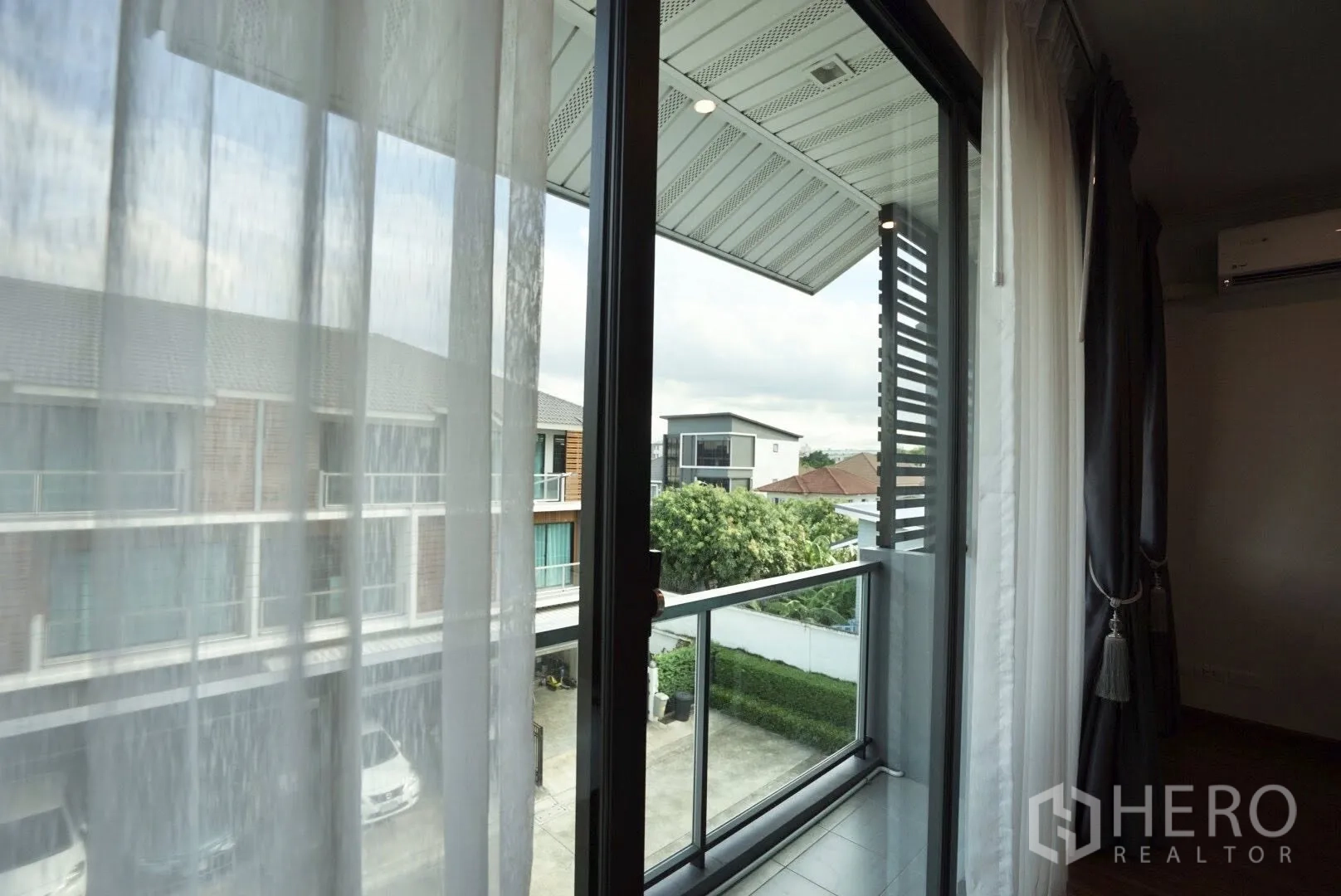 Townhouse for rent in Bang Kapi, Bangkok - View from the bedroom balcony across a quiet townhouse community with trees and parking below.