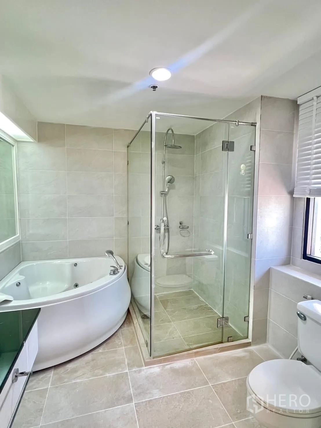 Condominium for rent in Khlong Toei, Bangkok - Bathroom with glass shower enclosure and corner whirlpool bathtub.