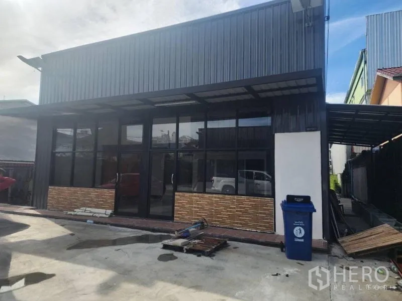 Warehouse for rent in Suan Luang, Bangkok - Angled exterior of the warehouse showing glass panels and a side carport.