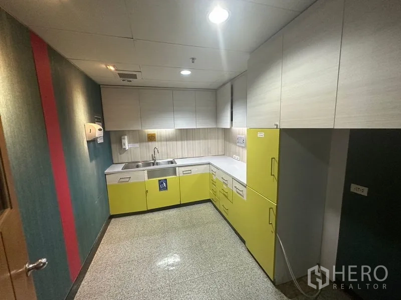 Office Space for rent in Khlong Toei, Bangkok - Compact kitchenette with L-shaped counters, sink and yellow lower cabinets.
