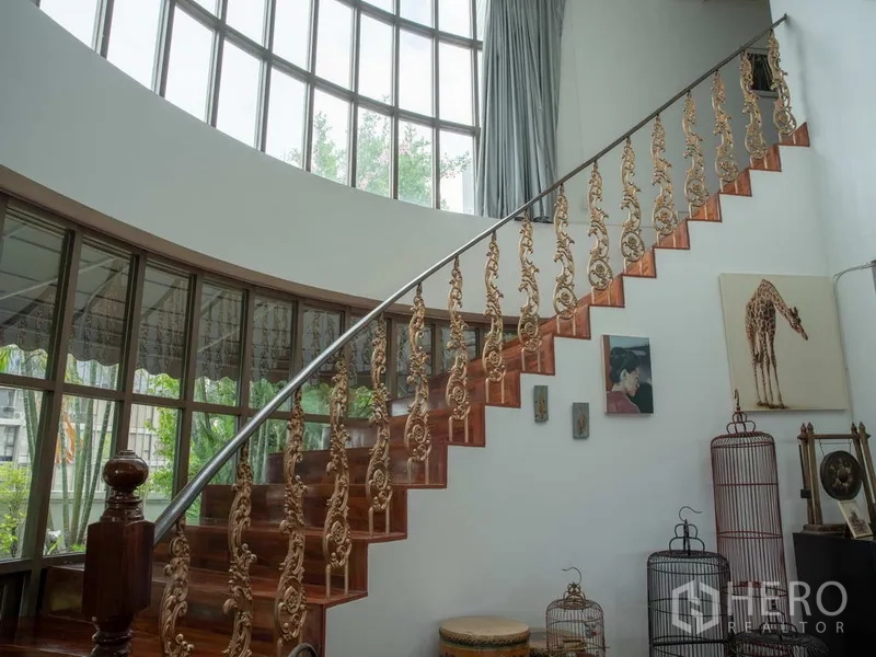 Apartment for rent in Khlong Toei, Bangkok - Curved wooden staircase with ornate gold balustrade and tall arched windows.