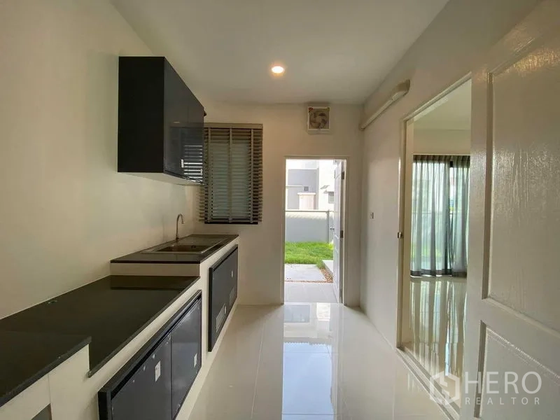 Detached House for rent in Don Mueang, Bangkok - Linear kitchen with upper cabinets, dual sink and door to the backyard.