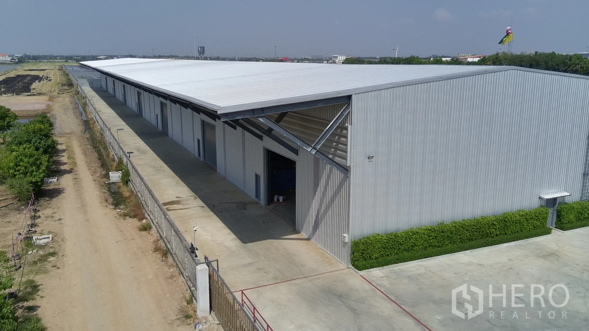 Warehouse for rent in Lam Luk Ka, Pathum Thani - Elevated exterior of the warehouse showing multiple bay doors and a perimeter fence.