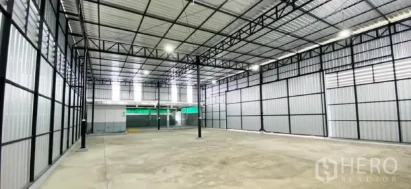 Warehouse for rent in Din Daeng, Bangkok - Wide-angle view of the open warehouse floor with metal walls, central columns, and bright skylights.