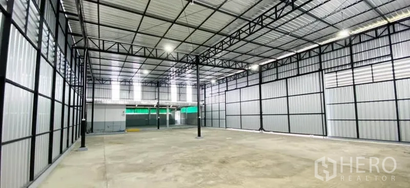 Warehouse for rent in Din Daeng, Bangkok - Wide-angle view of the open warehouse floor with metal walls, central columns, and bright skylights.