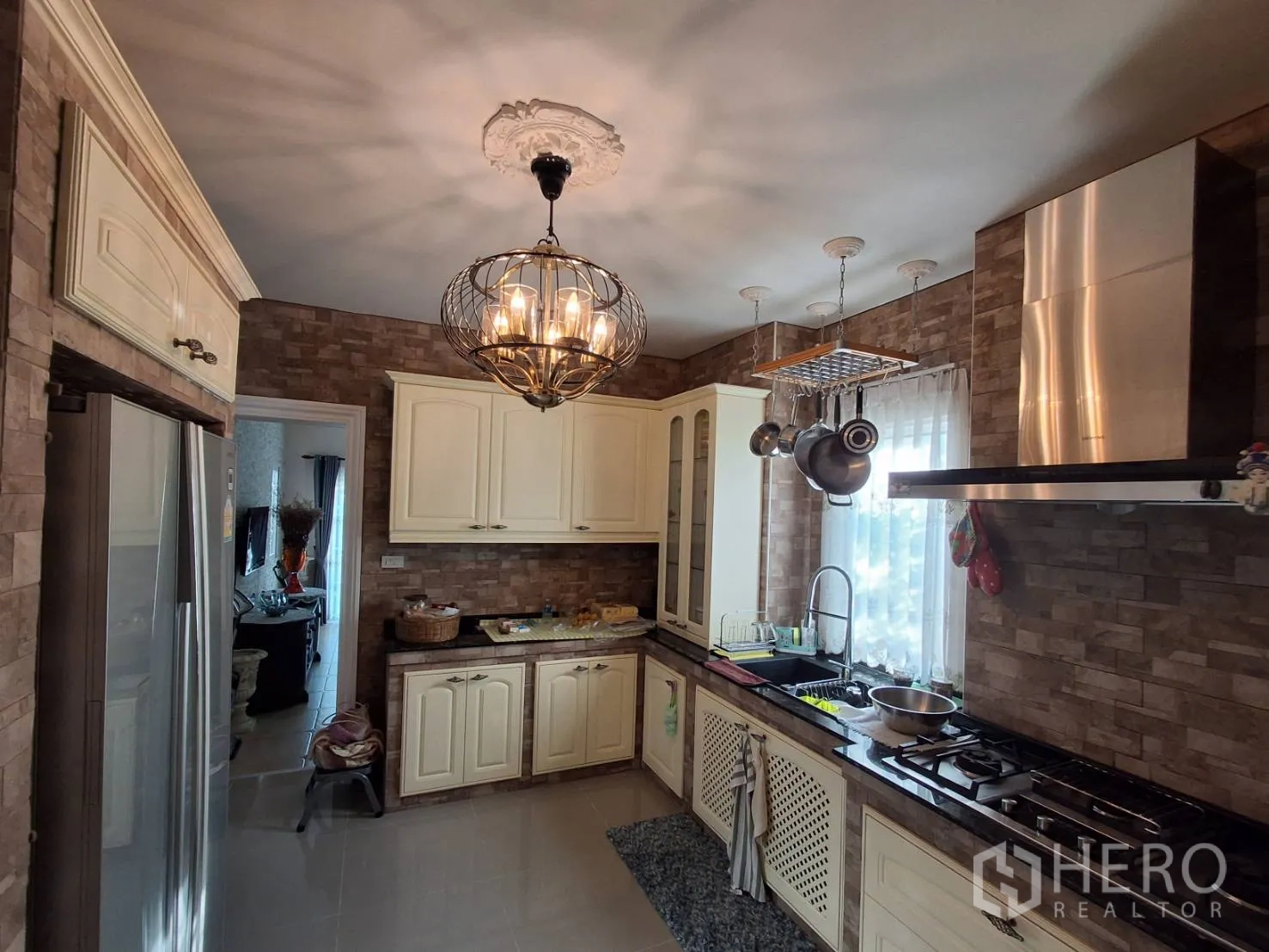 Detached House for rent or sale in Ban Chang, Rayong - Kitchen angle showing sink, hanging pot rack, gas cooktop and double-door fridge.