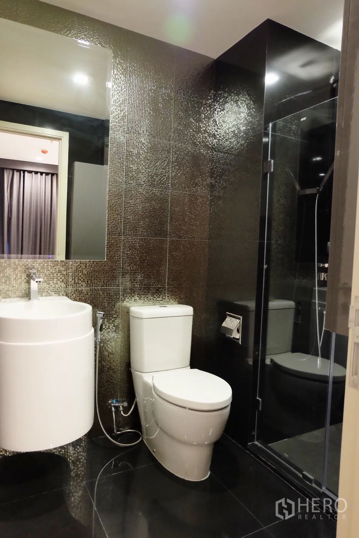 Condominium for rent in Khlong Toei, Bangkok - Stylish bathroom with mosaic tiles, round vanity sink, toilet and glass shower enclosure.