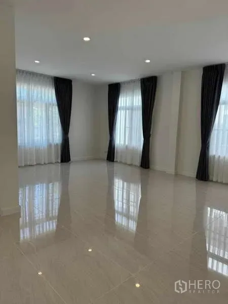 Detached House for rent in Samut Prakan - Bright open-plan living room with glossy floor tiles, recessed lighting, and tall curtained windows.