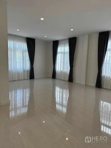 Detached House for rent in Samut Prakan - Bright open-plan living room with glossy floor tiles, recessed lighting, and tall curtained windows.