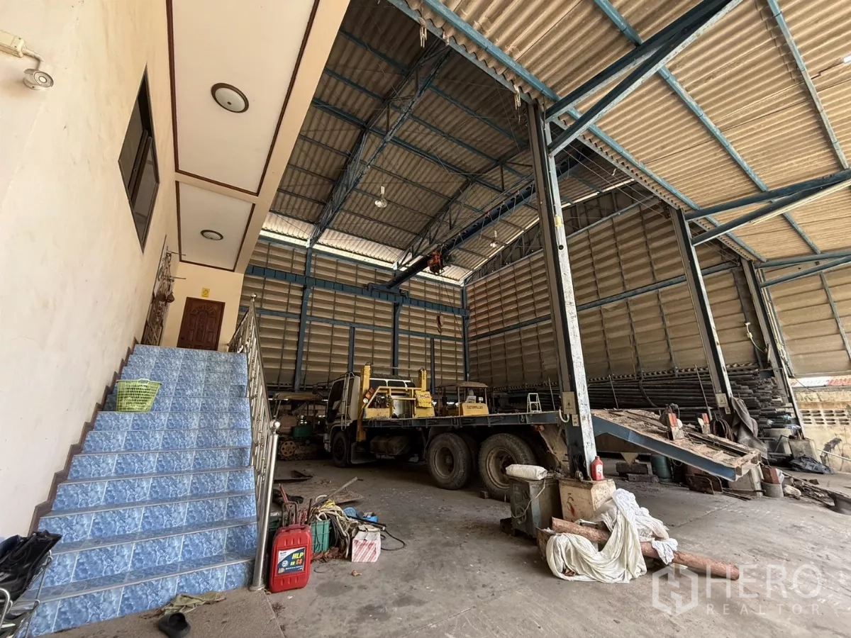 Warehouse for sale in Phra Samut Chedi, Samut Prakan - High‑bay warehouse bay with truck parked and staircase leading to mezzanine rooms.