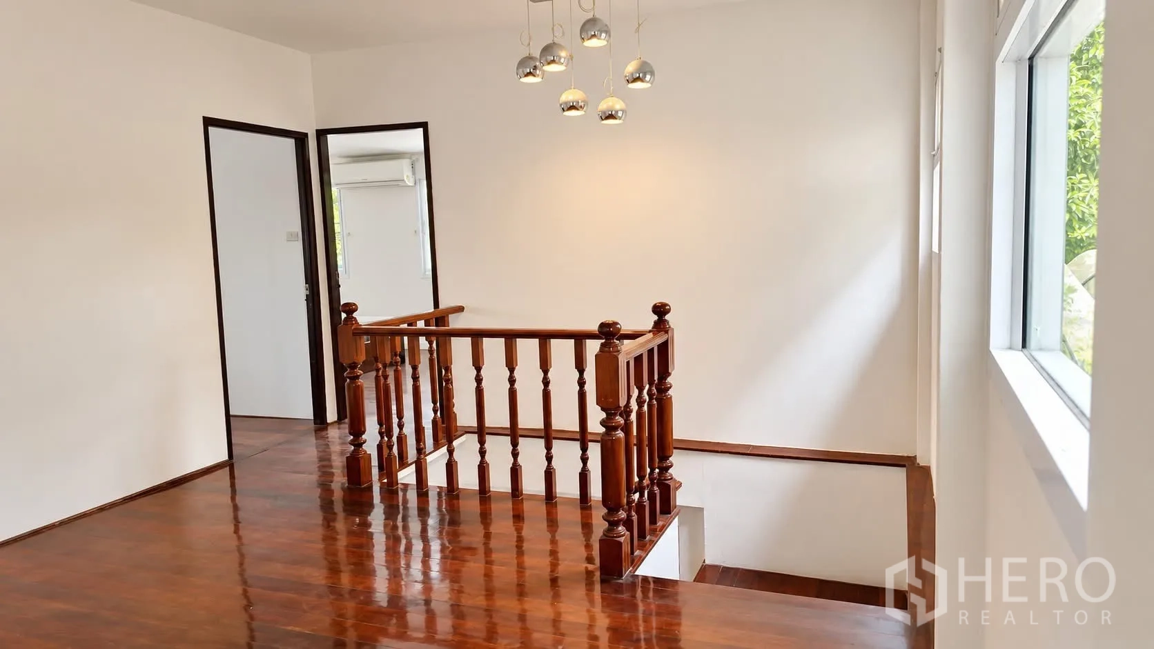 Detached House for rent in Khlong Toei, Bangkok - Upper landing with polished wooden stairs and floors beneath a modern pendant light.