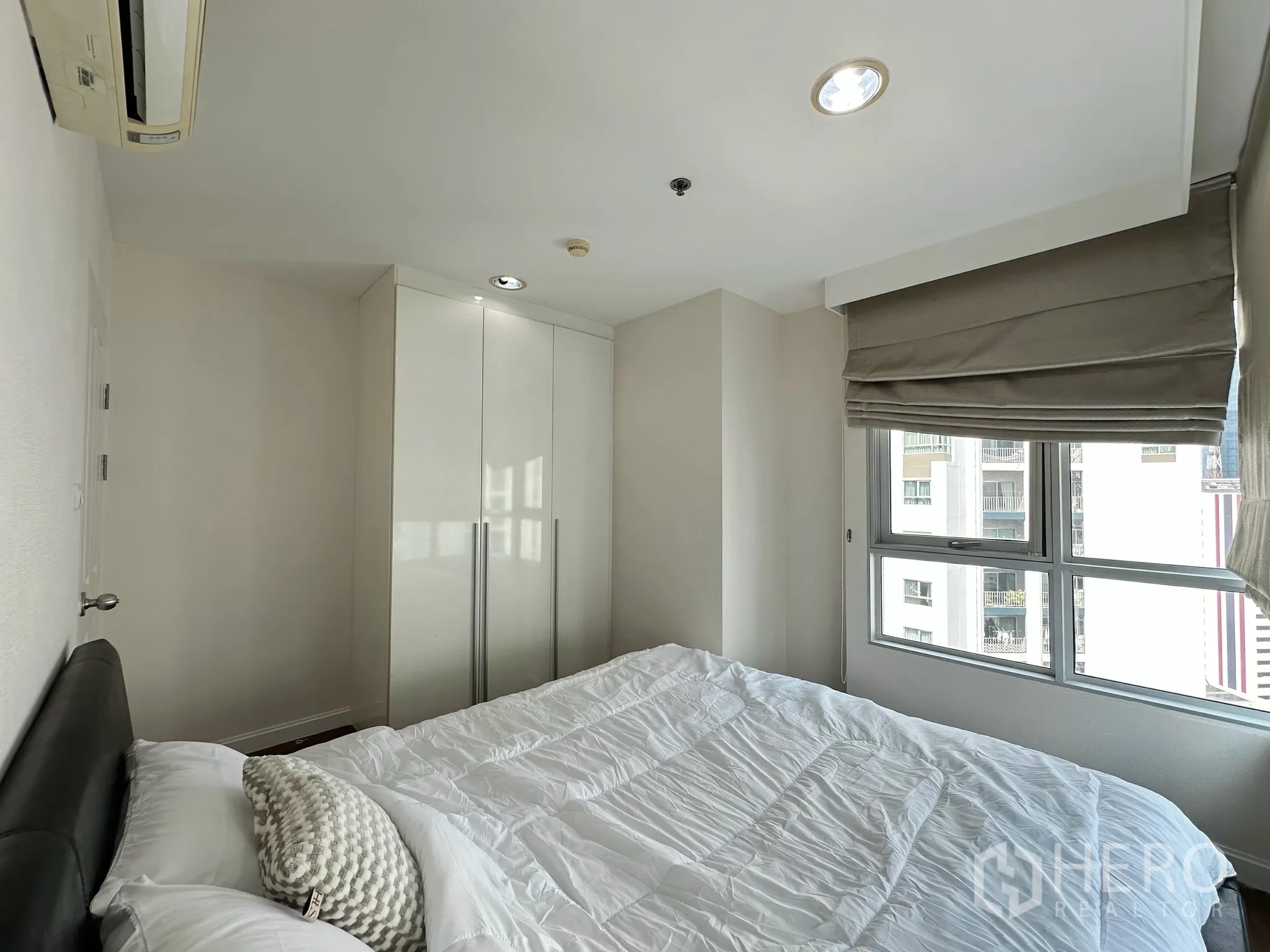 คอนโด for sale in Huai Khwang, Bangkok - ห้องนอนอบอุ่นมีเตียงติดหน้าต่าง ตู้เสื้อผ้าเงา และมุมมองตัวเมือง.