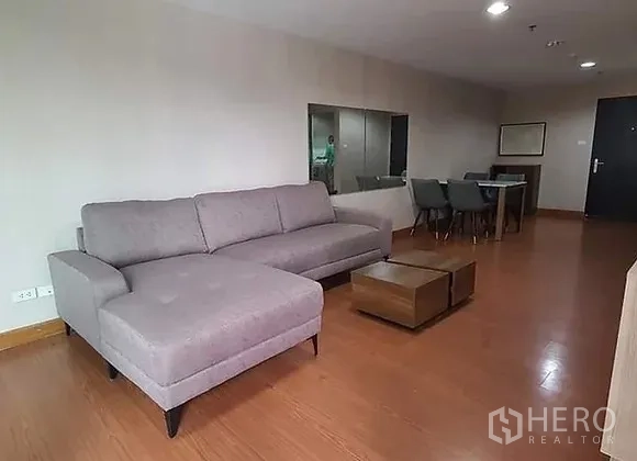Condominium for rent in Huai Khwang, Bangkok - Spacious living room with gray L-shaped sofa, wood floors, coffee tables and a dining area.